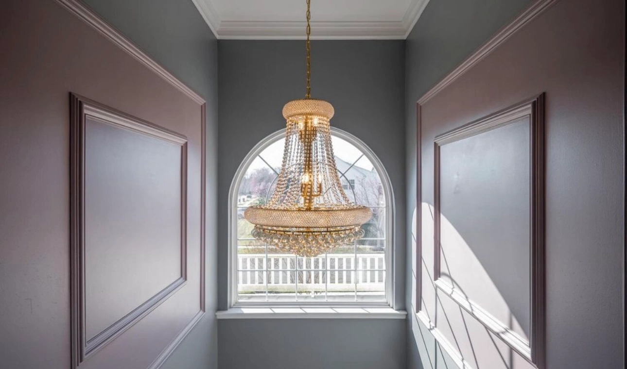 gold chandelier in between two grey walls with pink accents.