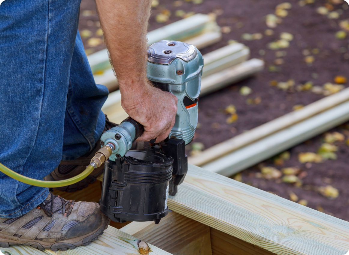 man fixing a deck by using a pressure nail gun.